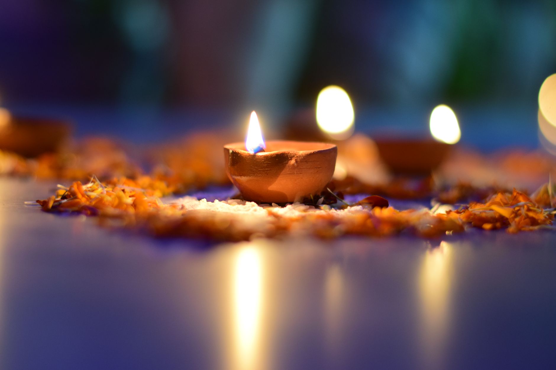 A warm and atmospheric close-up of a lit clay diya surrounded by flower petals.